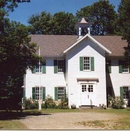 The Old Schoolhouse, a two-storey white clapboard building with a bell cupola and green shutters