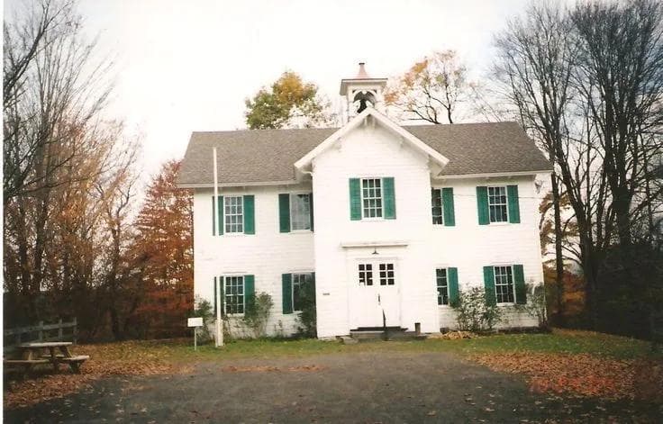 The schoolhouse seen across its grounds, showing the front double door and six-over-six windows